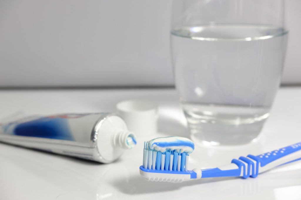 Brosse à dents, dentifrice et verre d'eau posés à côté sur un plan de travail