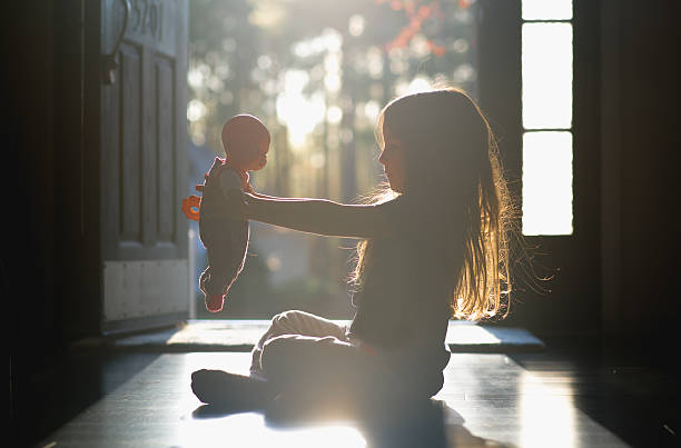 Petite fille assise par terre qui joue à la poupée